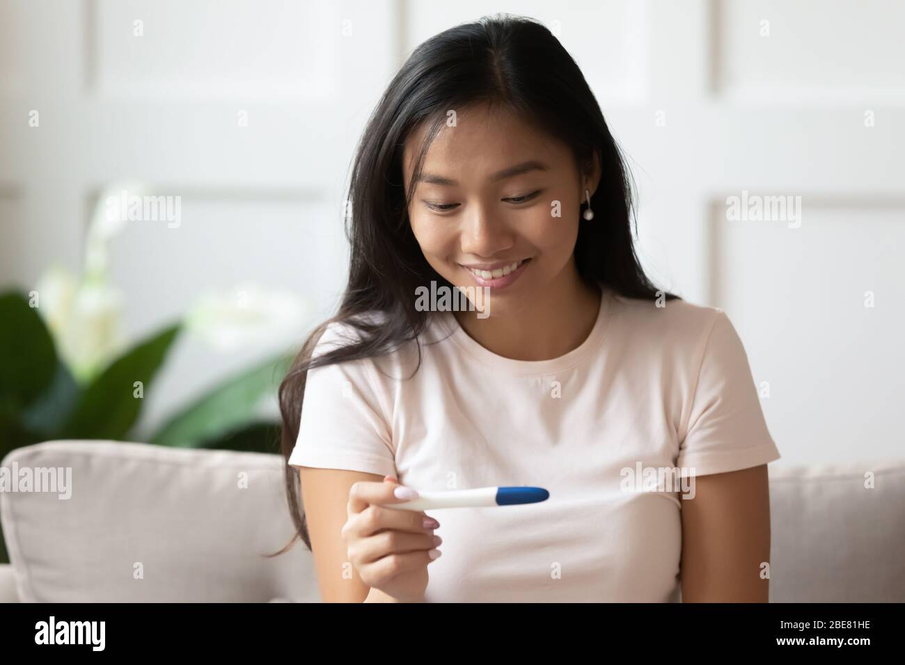 Asiatische Frau hält Schwangerschaftstest sehen zwei Streifen fühlt sich glücklich Stockfoto