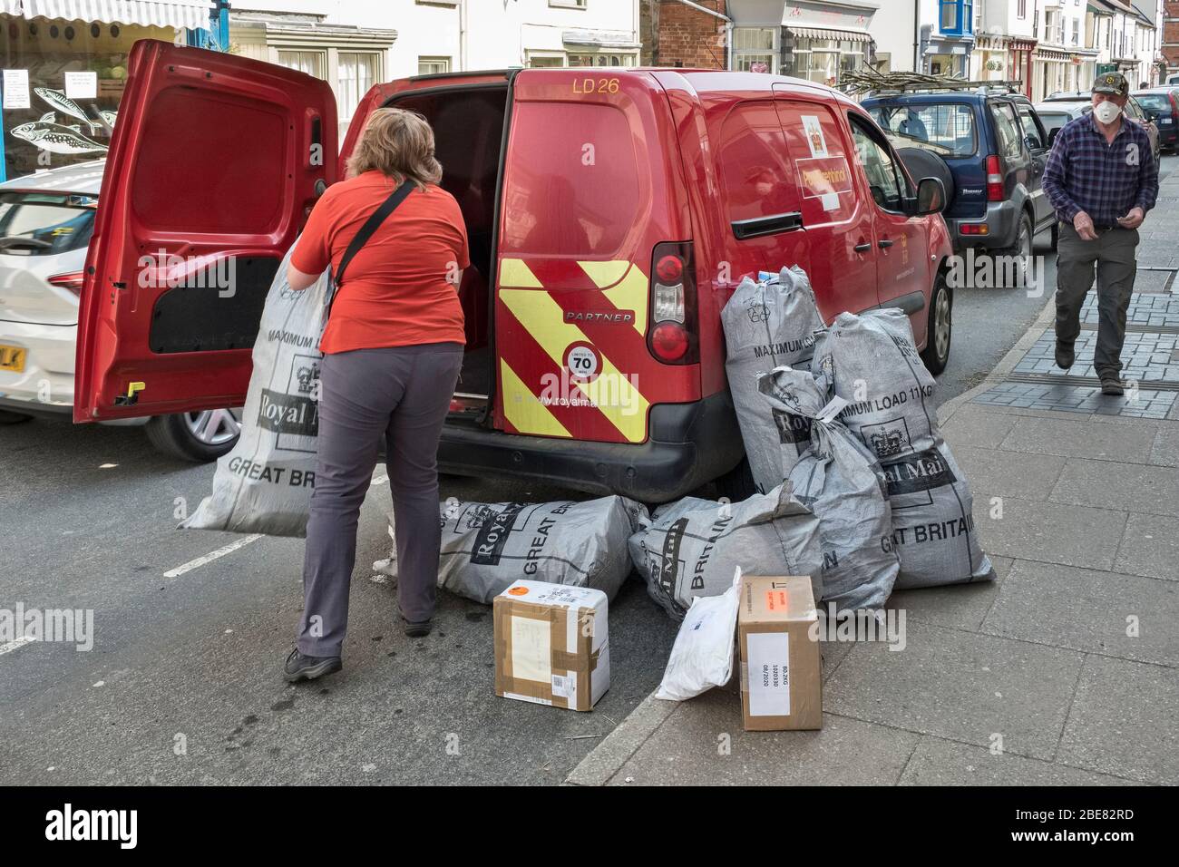Eine Postzustellerin, die während der Coronavirus-Pandemie schwere Postsäcke vom Postamt in Presteigne, Wales, Großbritannien, abholte Stockfoto
