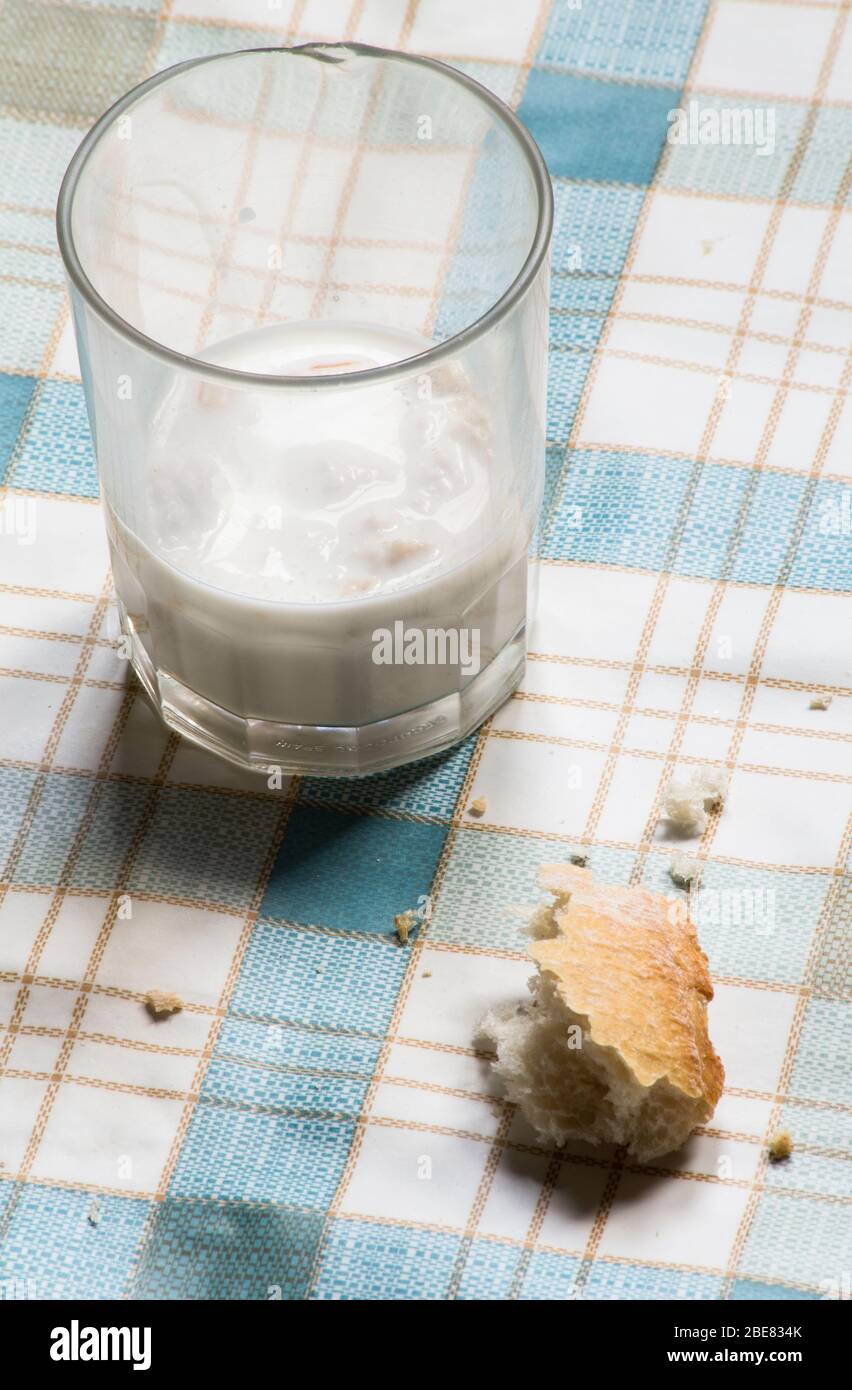 Ein Glas Milch mit einem Stück Brot, das die Armut widerspiegelt, die viele Menschen aufgrund einer Wirtschaftskrise durch das Coronavirus, CO, erleben können Stockfoto