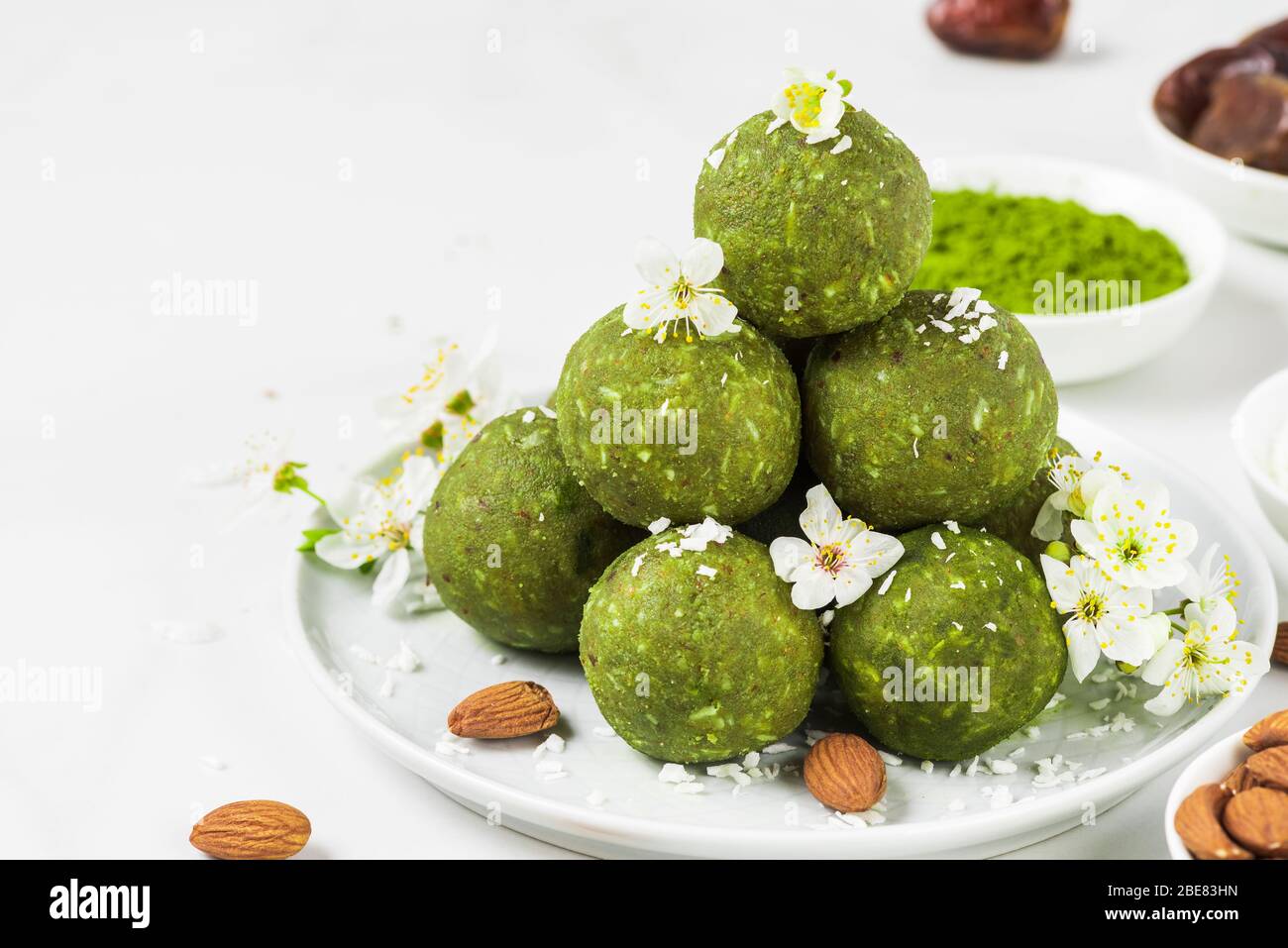 Grüne Matcha-Energiebälle oder Energiebisse aus Datteln und Nüssen mit Frühlingsblumen. Gesunde vegane Diät Snacks. Food Styling. Nahaufnahme mit Copy-SPAC Stockfoto