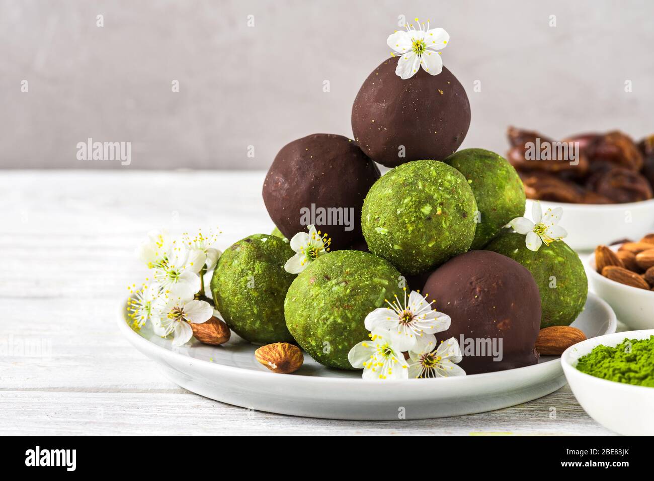 Grüne Matcha-Energiebälle oder Energiebeiße mit Energiebällen in Schokoladenglasur mit Frühlingsblumen. Gesunde vegane Diät Snacks. Food Styling. Nahaufnahme Stockfoto