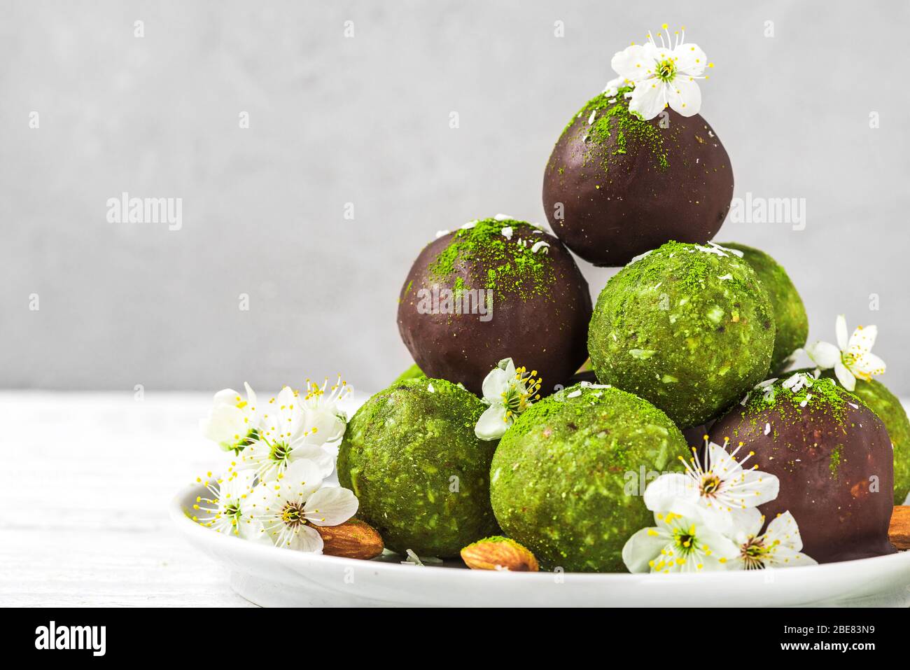 Rohes veganes hausgemachtes grünes Matcha-Dessert mit Matcha-Energiebällchen in Schokoladenglasur und Frühlingsblumen. Gesunde vegane Snacks Stockfoto