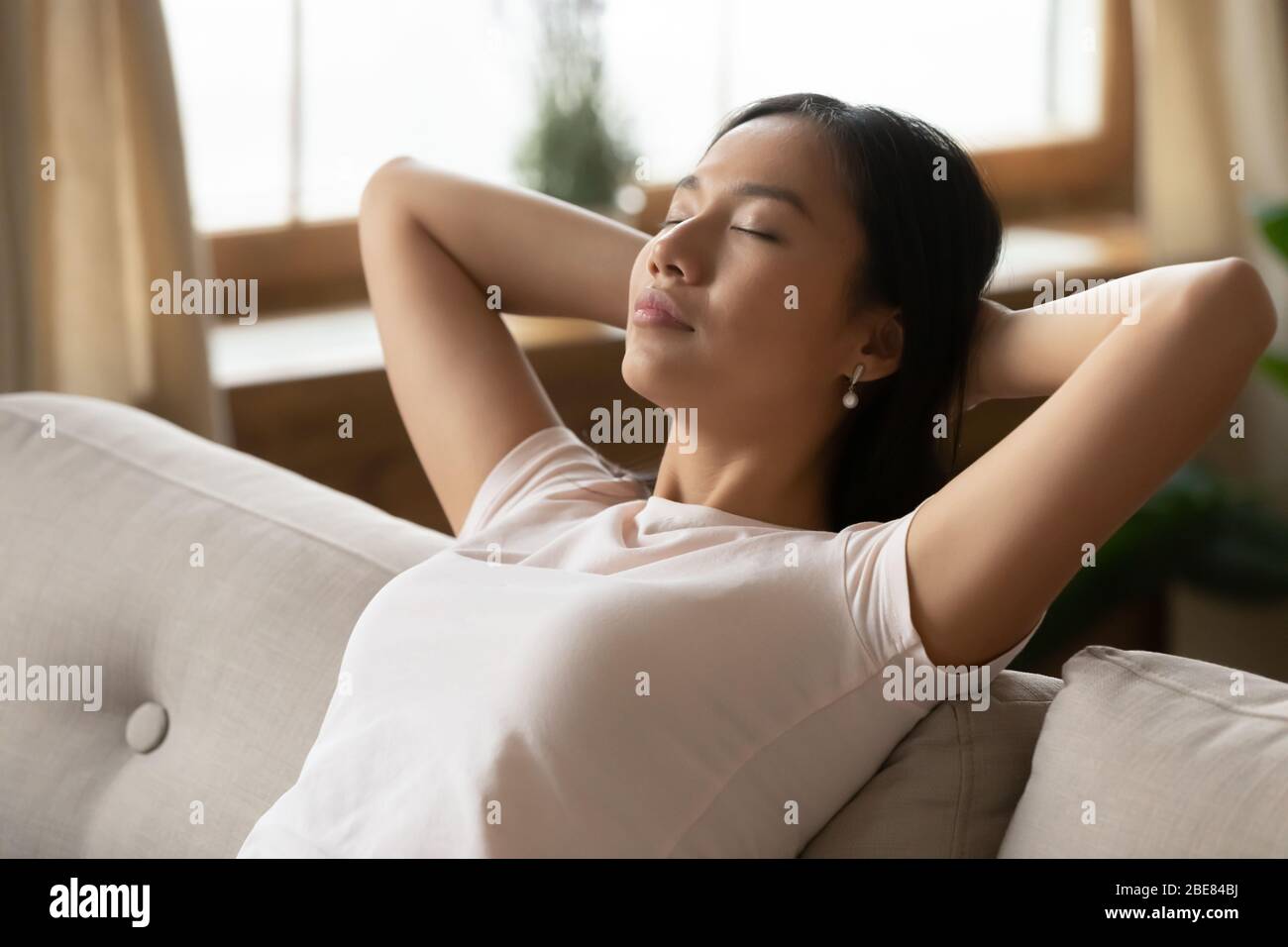 Asiatische Frau legte Hände hinter Kopf ruht auf Sofa Nahaufnahme Stockfoto