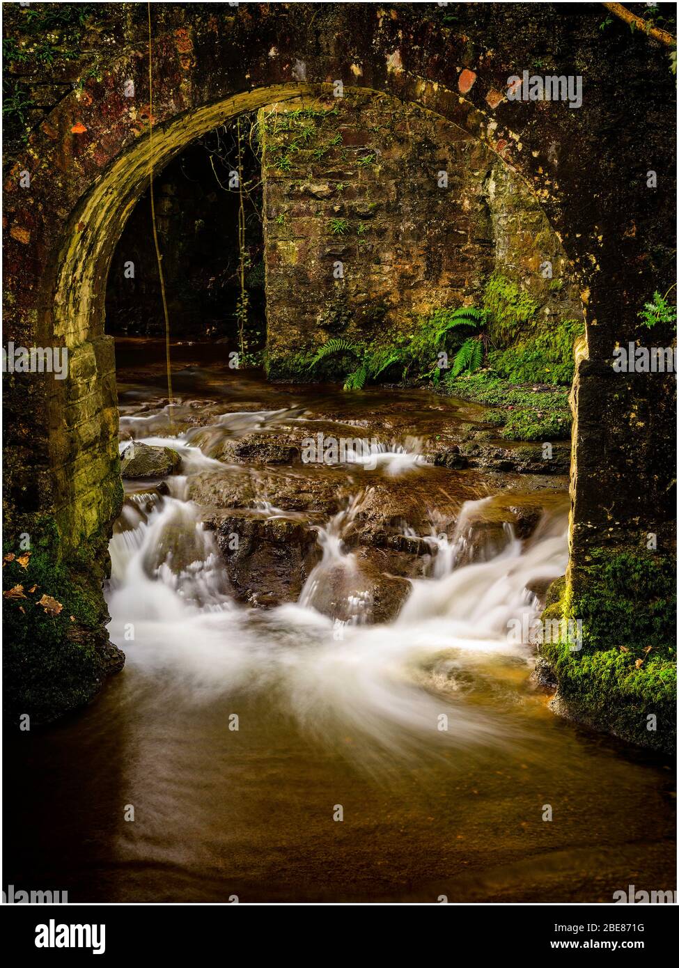 Torbogen unter einer alten Brücke über einen Bach Stockfoto