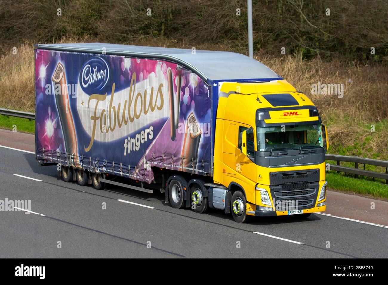 DHL International Versand Werbung Cadbury fabelhafte Finger; Gelbe Spedition Lieferwagen, LKW, Transport, Volvo FH LKW, Frachtführer, Fahrzeug, gewerblichen Transport, Industrie, M6 in Manchester, Großbritannien Stockfoto