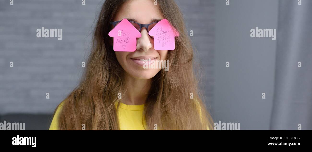 Frau mit rosa Aufkleber auf Brille mit Text zu Hause bleiben. Virenschutzkonzept sperren. Motivationszitat auf Aufklebern. Panorama-Banner Coronavirus Stockfoto