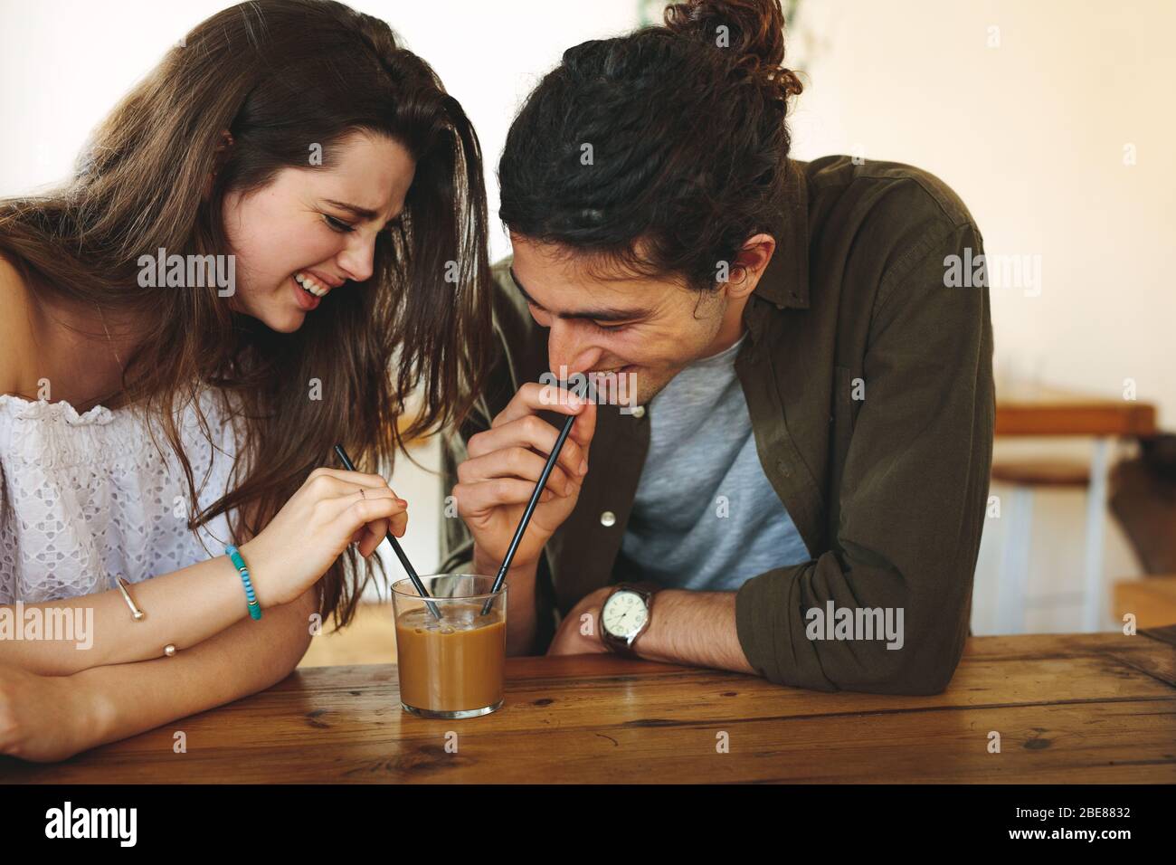 Ein glückliches junges Paar, das im Café verliebt ist und einen Kaffee aus demselben Glas trinkt. Junger Mann und Frau genießen einen Kaffee auf dem Tisch. Stockfoto