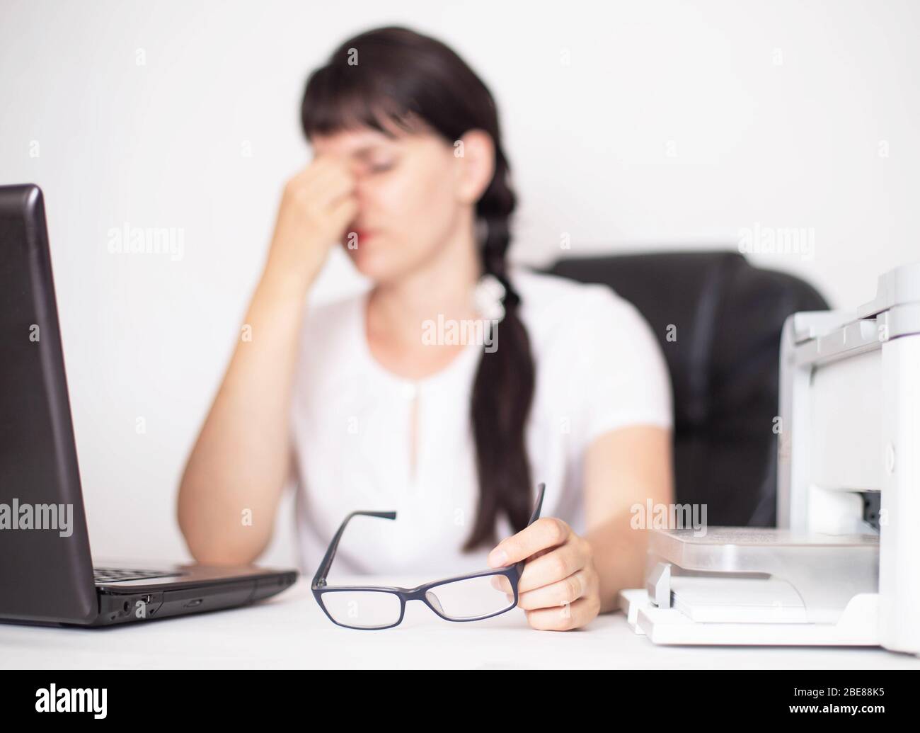 Mädchen Brünette Büroangestellte hält Augen. Das Konzept von Müdigkeit und Schmerzen in den Augen bei der Arbeit am Computer, Hintergrund Stockfoto