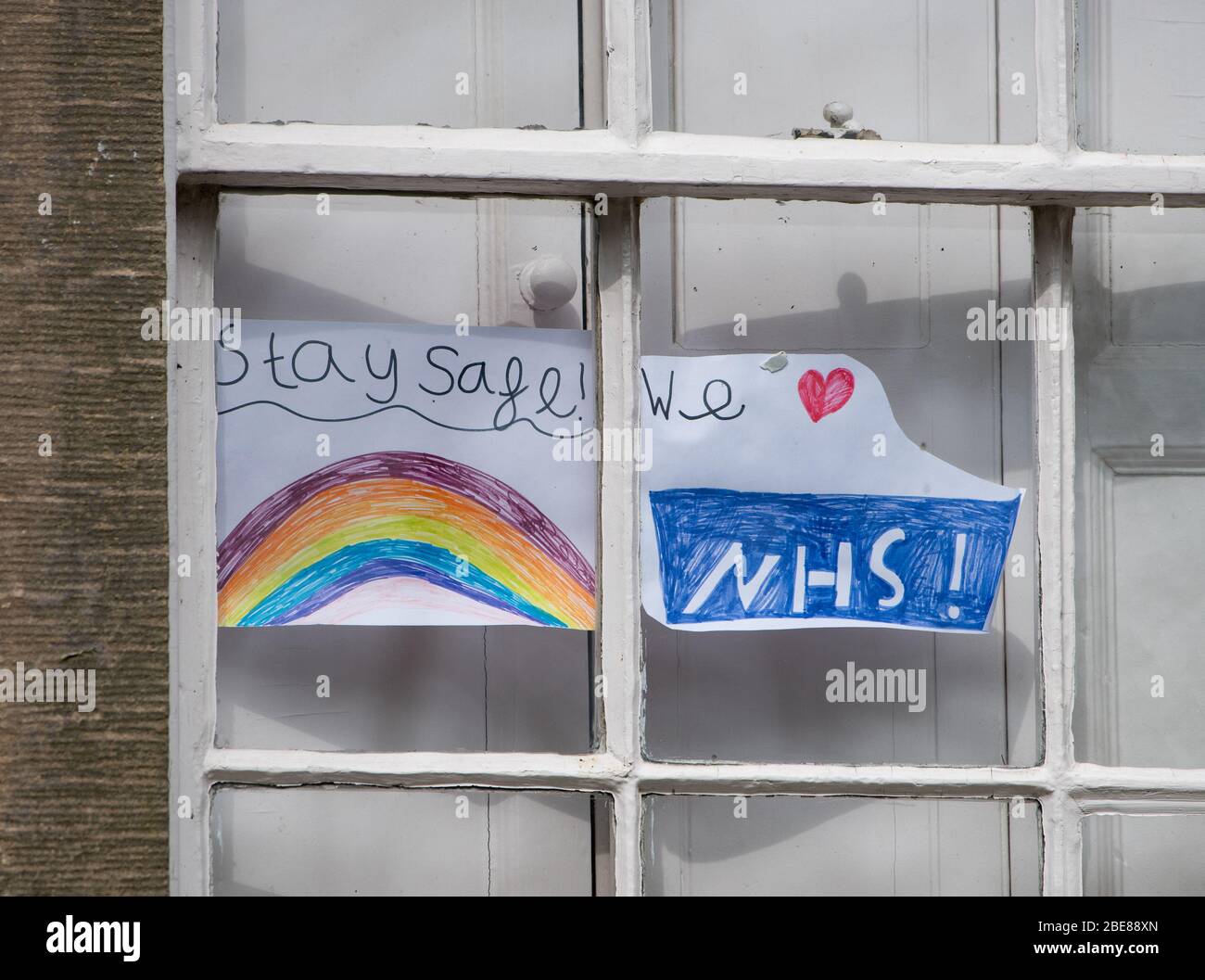 Ein Kind zeichnet einen Regenbogen, bleiben Sie sicher und NHS-Zeichen auf einem Fenster zur Unterstützung der National Health Service, Chipping, Preston, Lancashire, Großbritannien Stockfoto