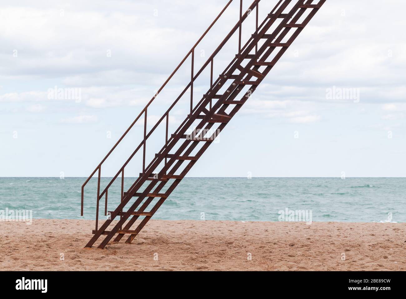 Rostige Metalltreppe am Sandstrand unter bewölktem Himmel Hintergrund Stockfoto