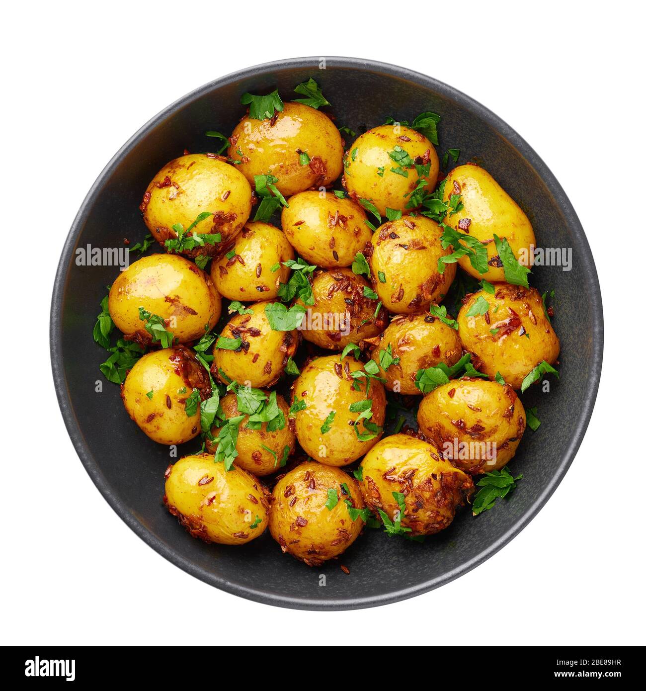 Jeera Aloo in schwarzer Schale isoliert auf weißem Hintergrund. Jeera Aloo ist ein Gericht der indischen Küche mit Babykartoffeln, Jeera-Samen und Koriander. Isolieren. Oben V Stockfoto