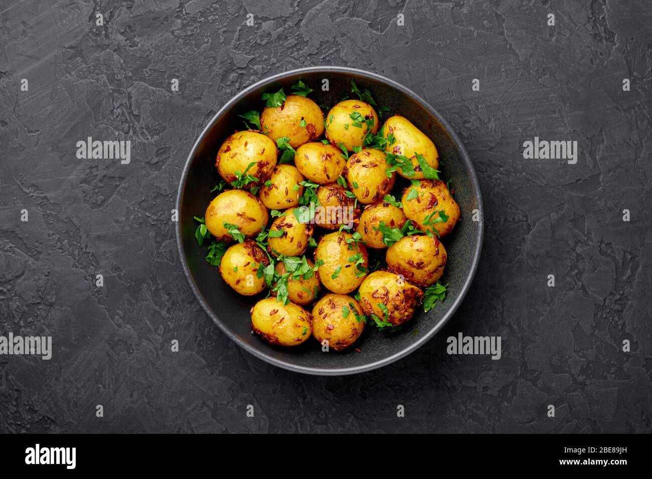 Jeera Aloo in schwarzer Schale auf dunklem Schiefergrund. Jeera Aloo ist ein Gericht der indischen Küche mit Babykartoffeln, Jeera-Samen und Koriander. Kopierbereich Stockfoto