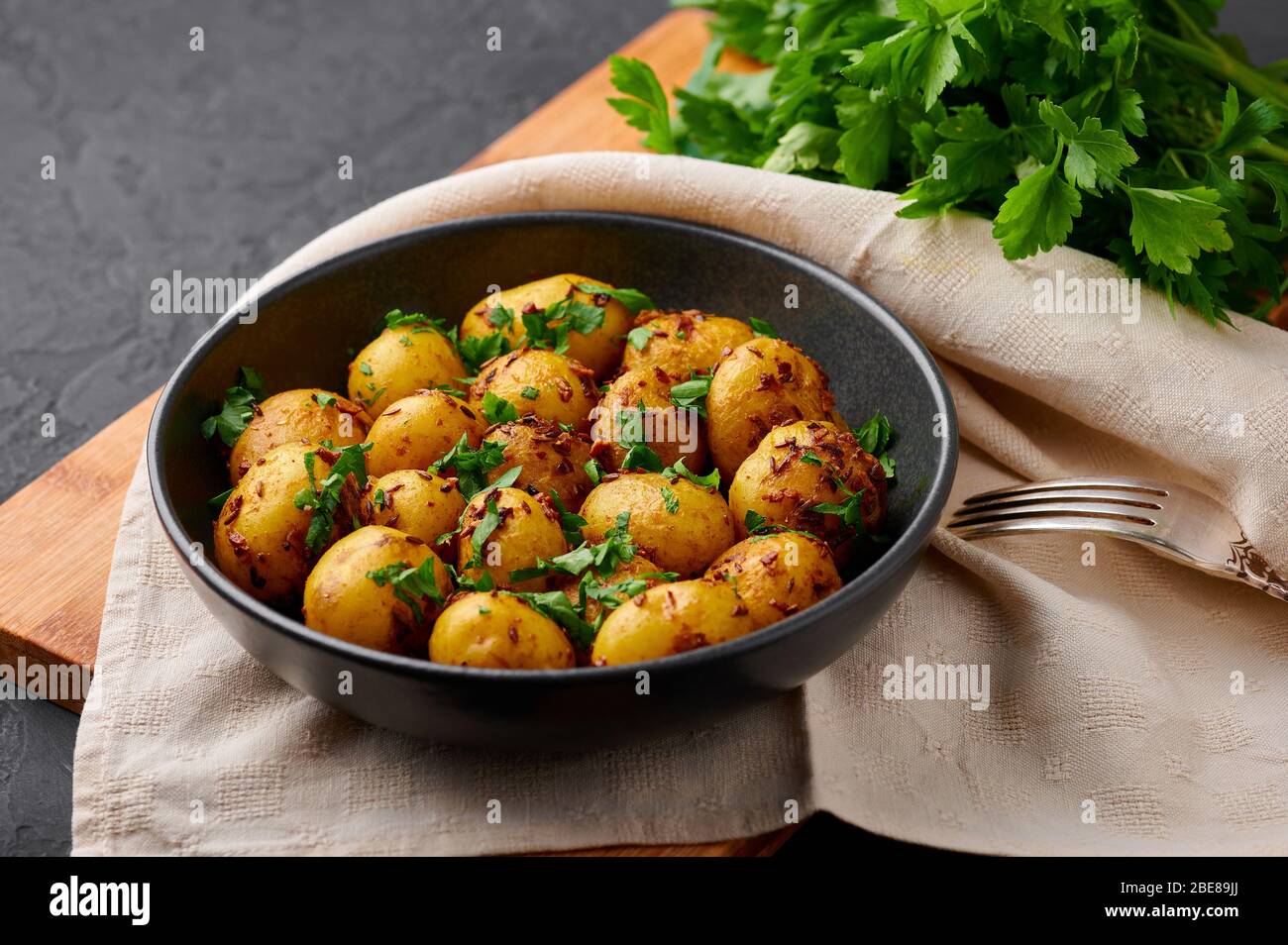 Jeera Aloo in schwarzer Schale auf dunklem Schiefergrund. Jeera Aloo ist ein Gericht der indischen Küche mit Babykartoffeln, Jeera-Samen und Koriander. Stockfoto