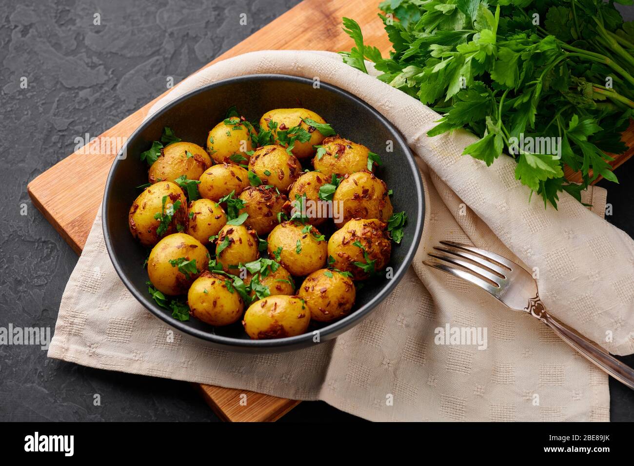Jeera Aloo in schwarzer Schale auf dunklem Schiefergrund. Jeera Aloo ist ein Gericht der indischen Küche mit Babykartoffeln, Jeera-Samen und Koriander. Stockfoto
