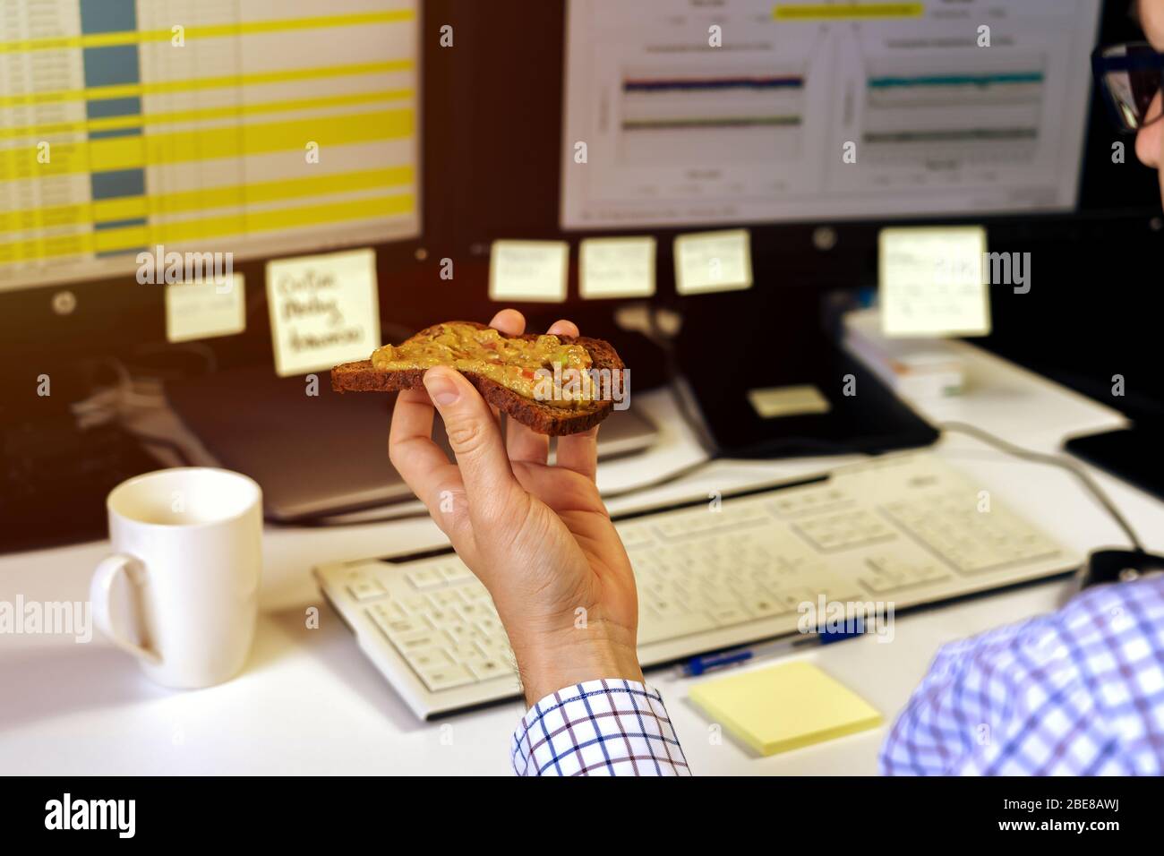 Geschäftiger Geschäftsmann, der während der Arbeit am Computer in Eile ein gesundes Avocado-Toast-Frühstück isst Stockfoto
