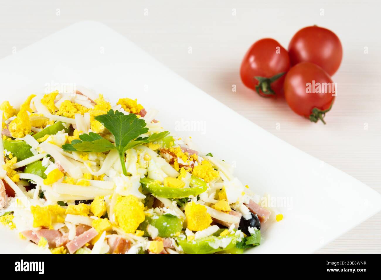 Traditioneller bulgarischer Schäferhund-Salat mit Tomaten, Paprika, Gurken, Pilzen, Schinken, Käse und Eiern in weißer Schüssel auf weißem Holztisch. Bulgarisch Stockfoto