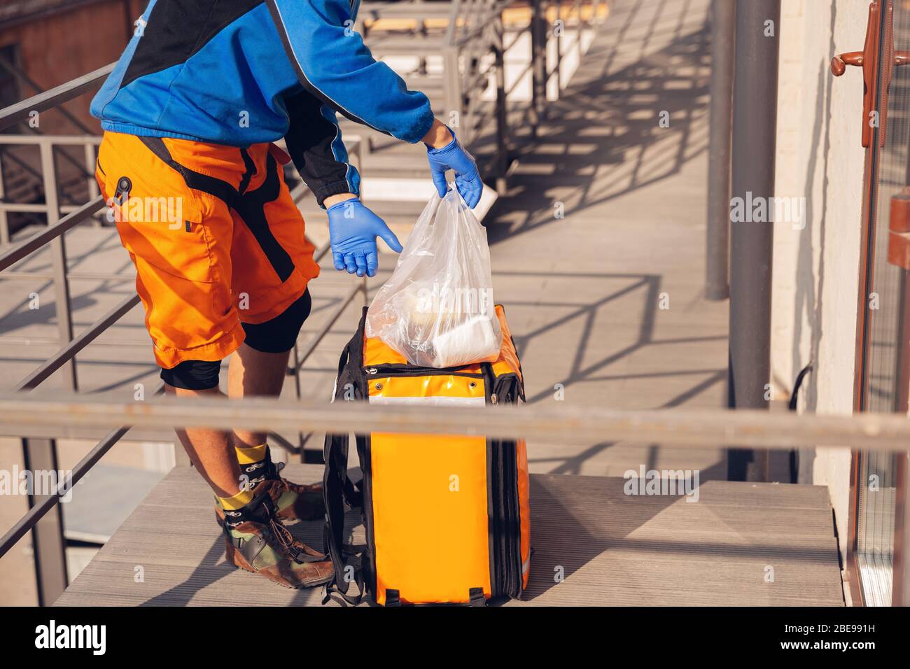 Kontaktloser Lieferservice während der Quarantäne. Man liefert Lebensmittel und Einkaufstaschen während der Isolation. Klopft an die Tür und lässt die Ware, bis der Kunde sie abholt. Sicherheit, Empfang, Distanz halten. Stockfoto