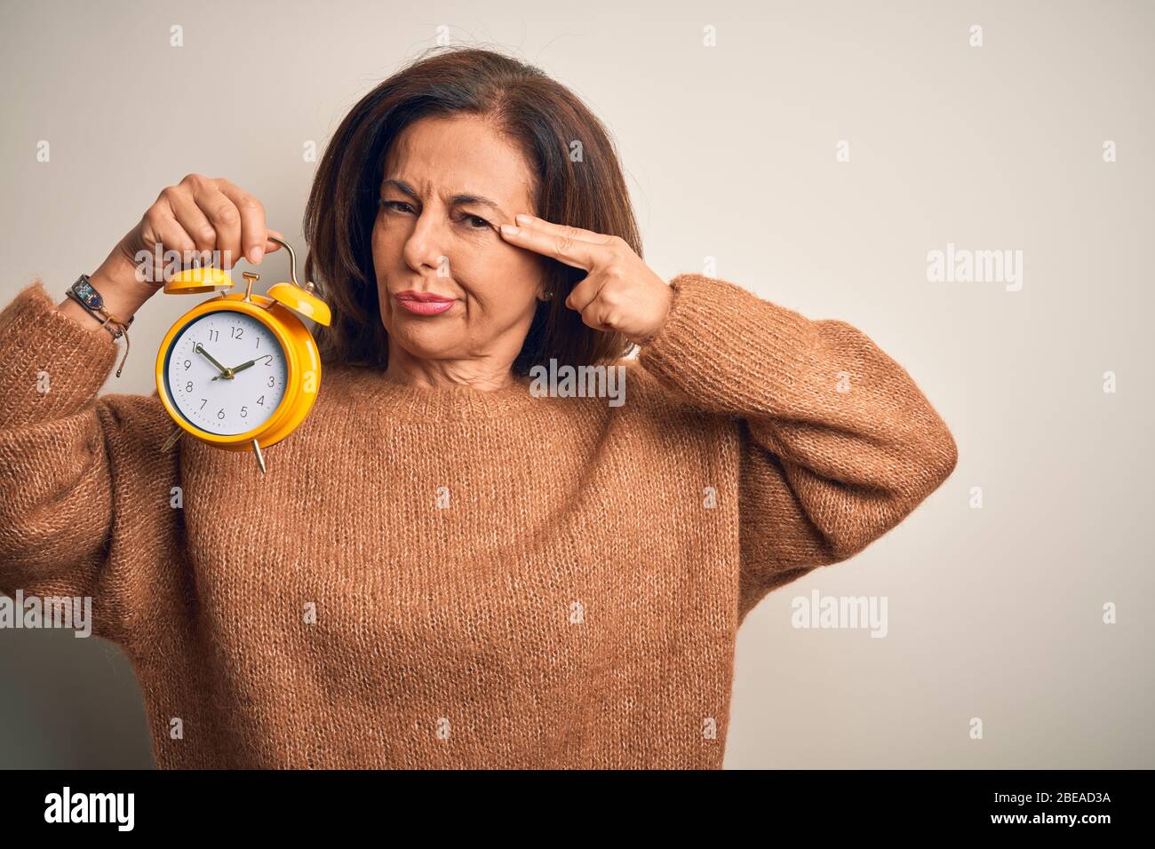 Mittlere Alter Brünette Frau, die klasischen Wecker über isolierten Hintergrund Shooting und Tötung selbst Zeigen Hand und Finger zu Kopf wie Waffe, Stockfoto