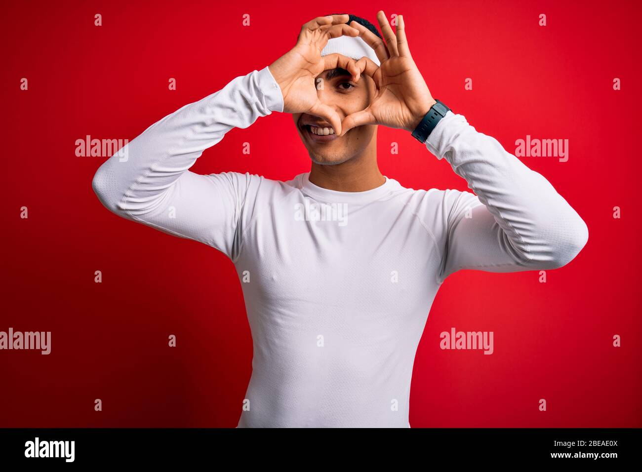 Junge gut aussehende afroamerikanischen Sportler tragen Sportbekleidung über rotem Hintergrund tun Herzform mit Hand und Finger lächelnd Blick durch Zeichen Stockfoto