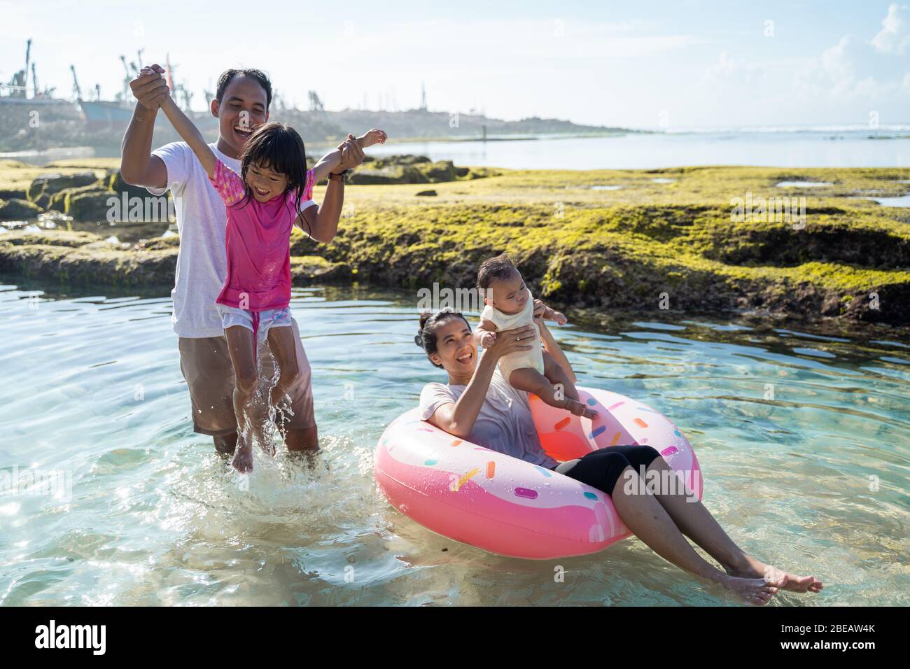 asiatische Glück Familie am Strand spielen, Mutter hält das Baby reiten eine schwimmende Ring Boje im Wasser Stockfoto