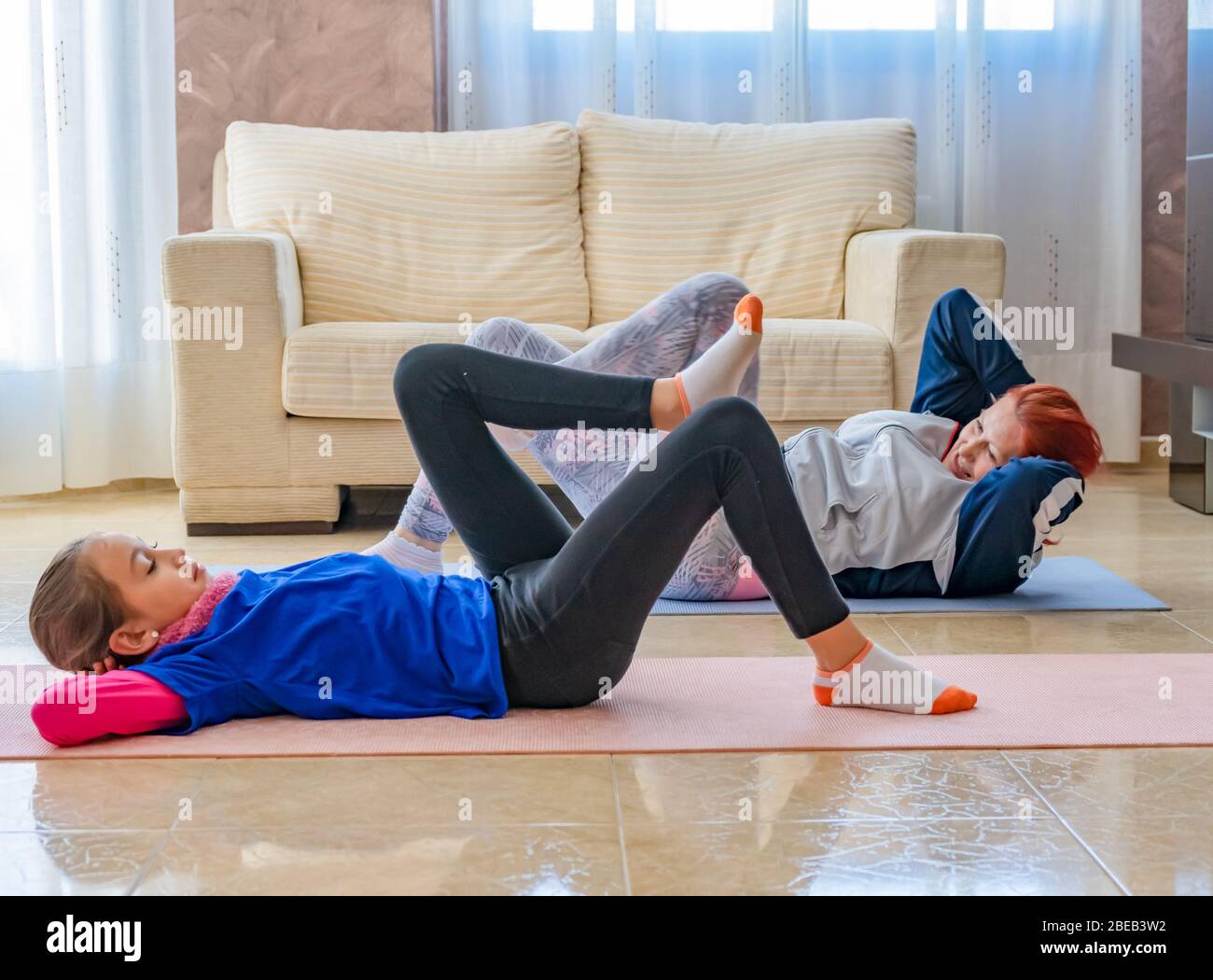 Mutter und Tochter in Sportkleidung Sport unter den weißen Sofas im Wohnzimmer zu Hause. Gesundes Leben Konzept Stockfoto