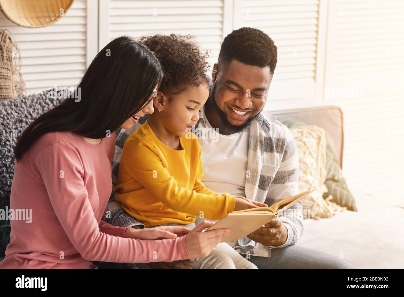Lächelnde internationale Eltern lehren das Kind zu lesen Stockfoto