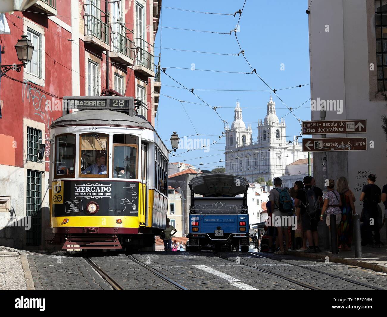 Die ikonische Straßenbahn Nummer 28, die man auf den belebten Straßen von Lissabon mit der Kathedrale im Hintergrund sieht. Stockfoto