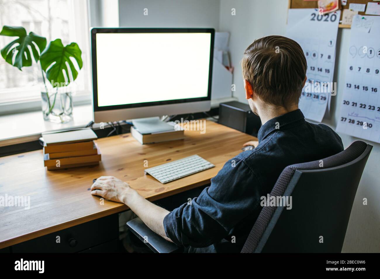 Mann, der vom Heimbüro aus arbeitet. Computer mit leerem leeren Bildschirm für Kopierspeicher und Informationen. Geschäftsmann aus der Hinteransicht. Eine Kreative Stockfoto