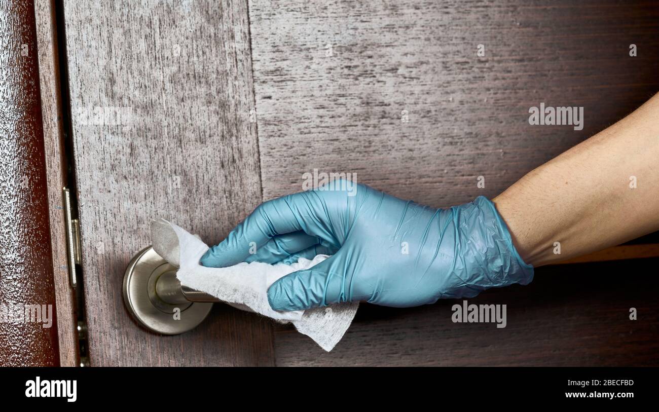 Reinigen, desinfizieren, den Türgriff aus Chrom mit einer Hand im Handschuh und Serviette ganz nah abwischen. Stockfoto