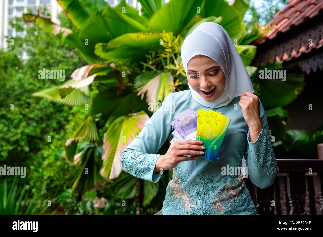 Ein Porträt der jungen malaiischen Frau mit überraschenden glücklichen Ausdruck, die einen Umschlag Taschengeld oder raya angpao der malaysischen Währung hält. Übersetzung Stockfoto