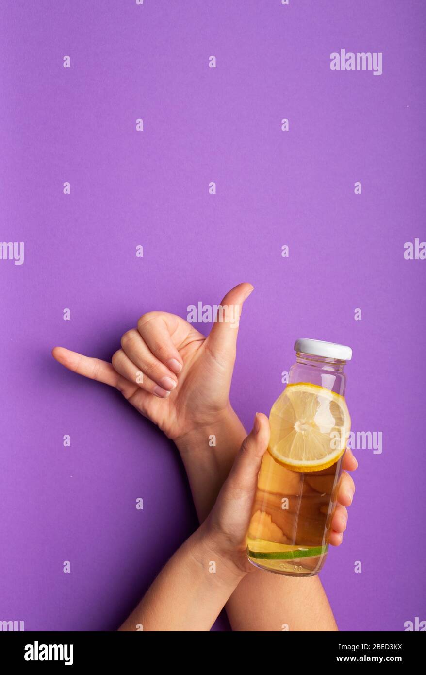 Frau, die Zitronendetox in einer Glasflasche auf violett präsentiert Stockfoto