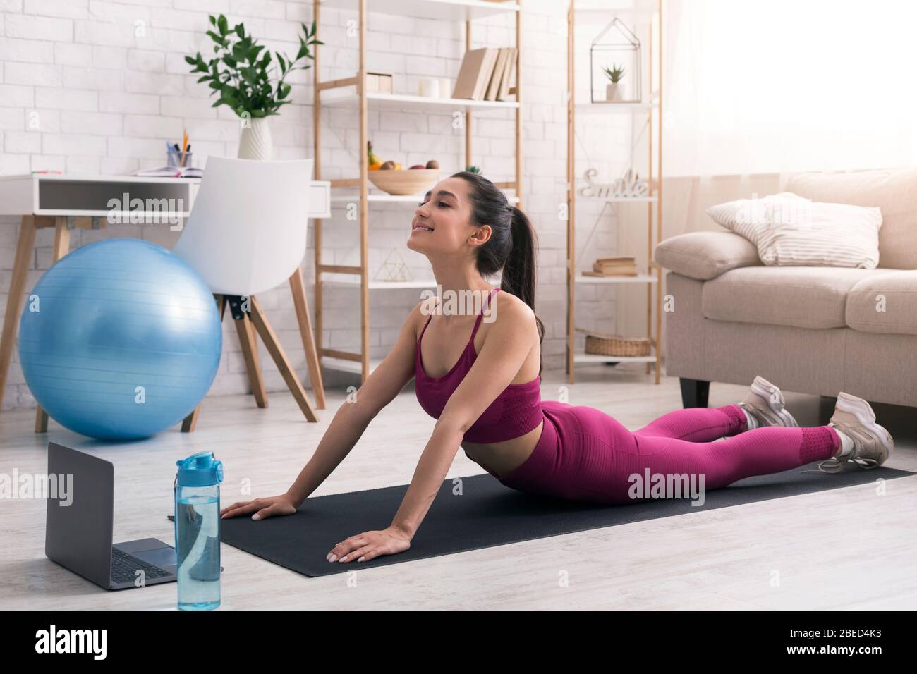 Bleiben Sie zu Hause Fitness. Junges Mädchen tun zurück biegen oder Schlange Yoga Pose in der Nähe Laptop drinnen Stockfoto