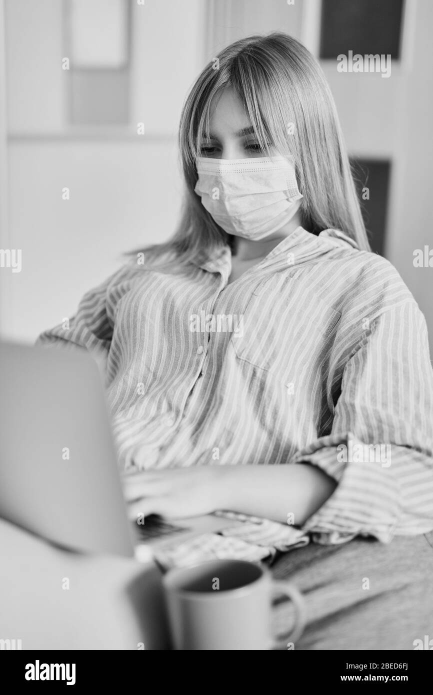 Attraktiver Teenager in einer medizinischen Maske, Pyjama sitzt auf einem Sitzsack zu Hause in Quarantäne. Konzept des Online-Studierens, Arbeitens oder Chatten über Isolation Stockfoto