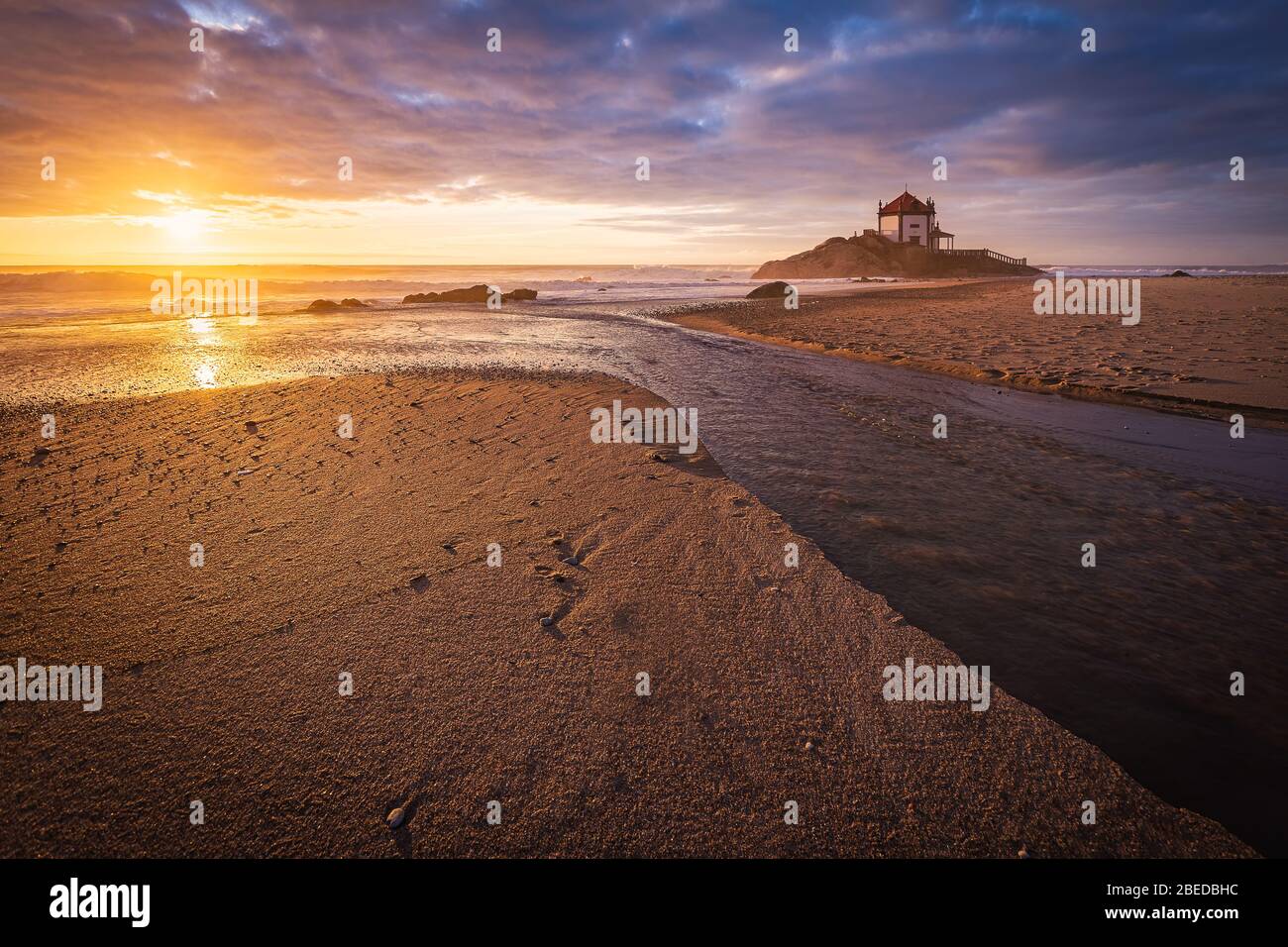 Schöne Kirche am Strand. Capela Senhor da Pedra, bei Sonnenuntergang, mit Wellen über der Kirche Stockfoto