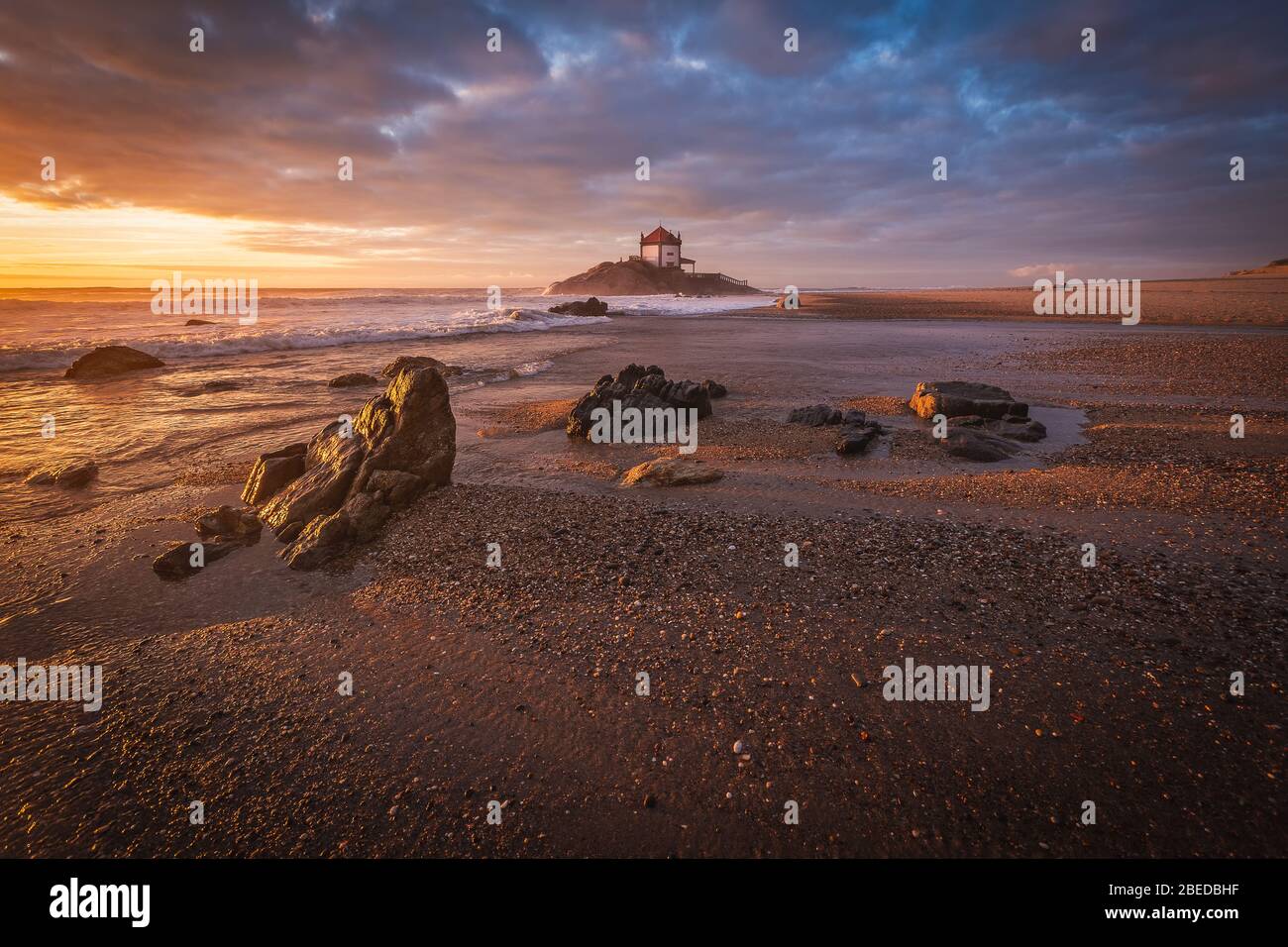 Schöne Kirche am Strand. Capela Senhor da Pedra, bei Sonnenuntergang, mit Wellen über der Kirche Stockfoto