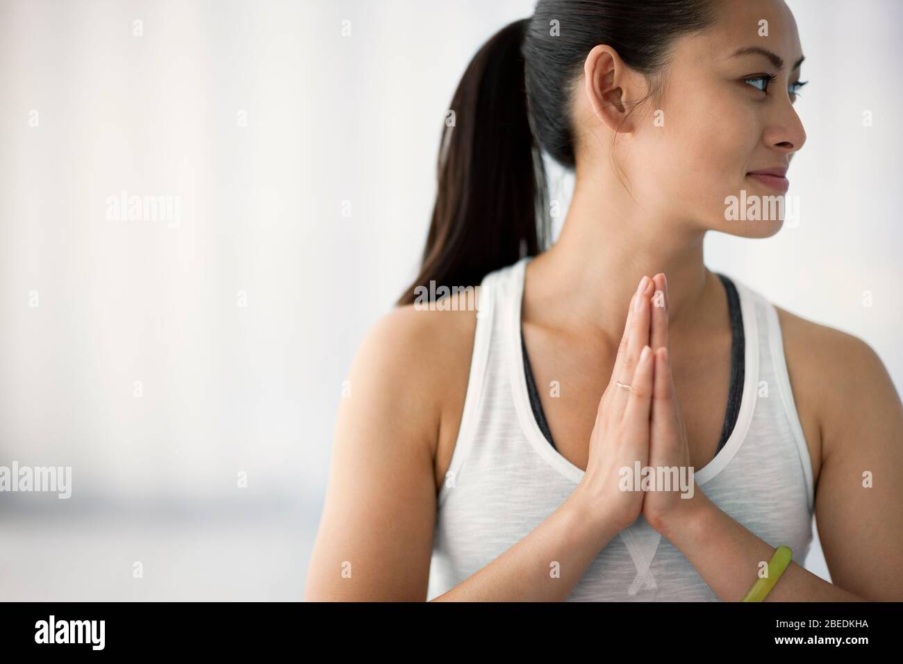Glückliche junge Frau, die mit ihren Händen in einer Yoga-Pose zusammen steht Stockfoto