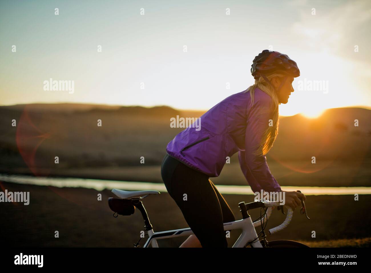 Junge Frau, die bei Sonnenuntergang eine Landstraße entlang fährt Stockfoto