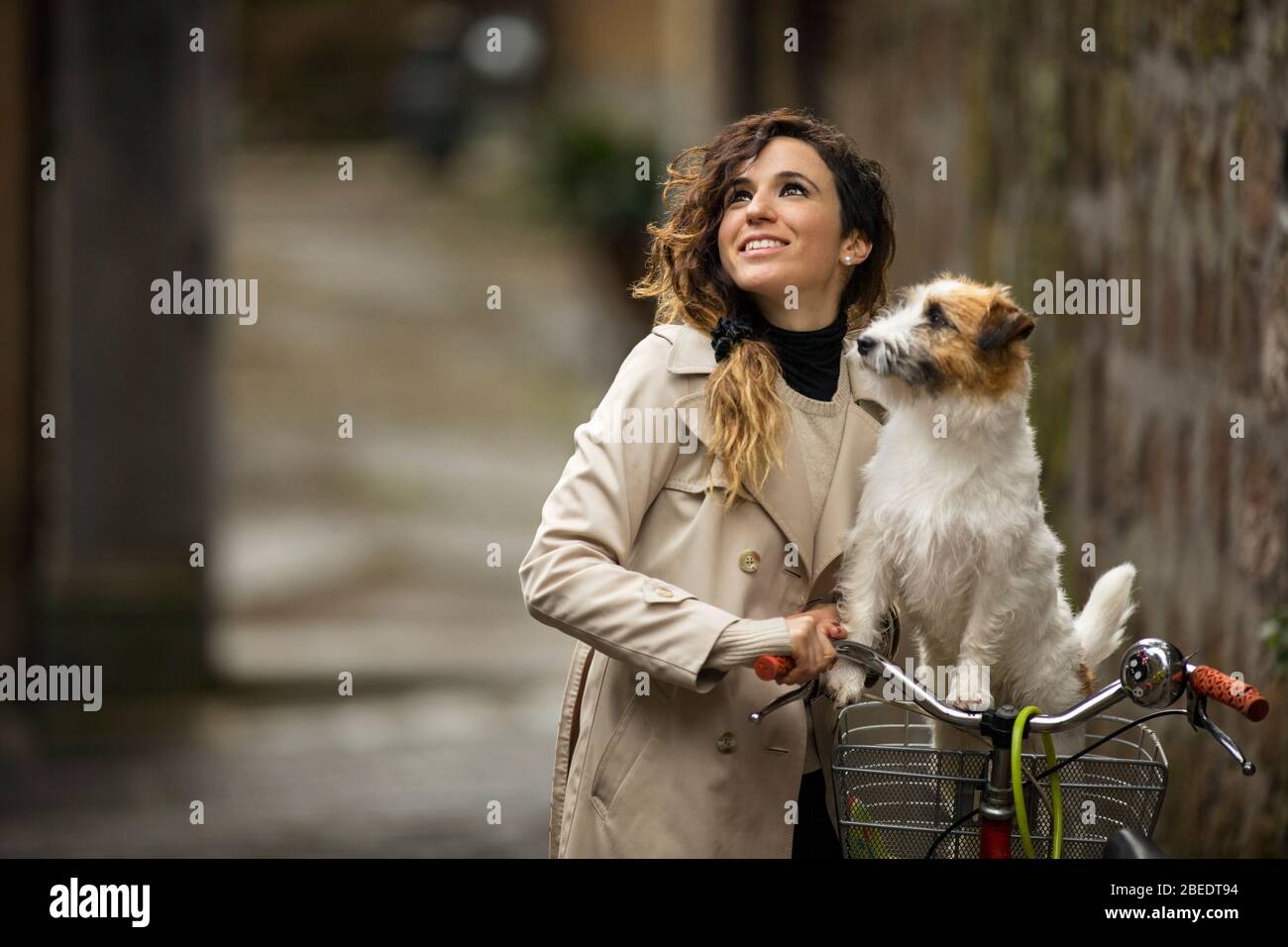 Glückliche junge Frau, die neben ihrem Fahrrad steht und einen Hund im Korb hat Stockfoto