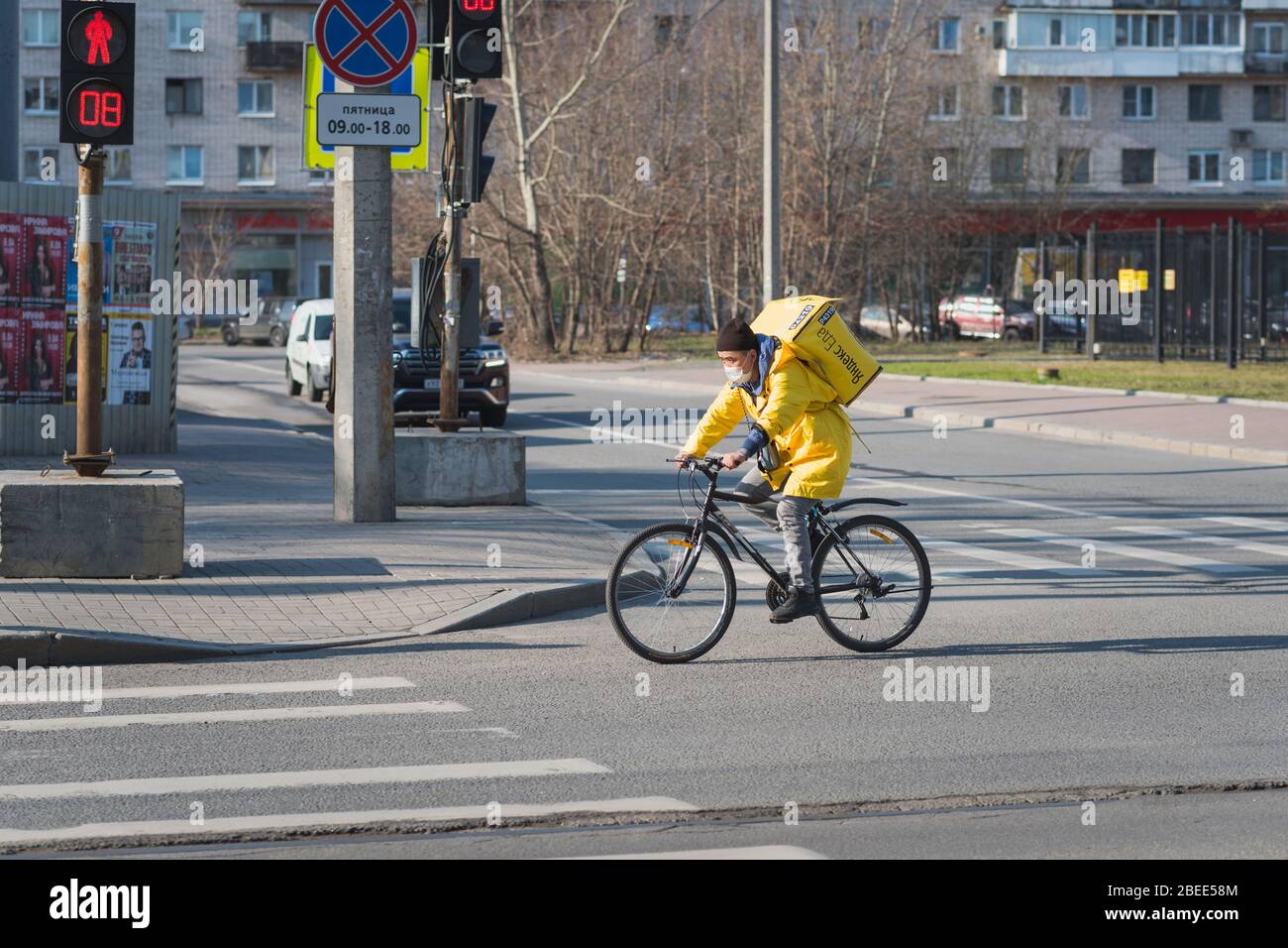 Sankt Petersburg, Russland - 7. April 2020: Ein Radfahrer in gelber Uniform trägt eine Kiste des Restaurants "Yandex EDA". Stockfoto