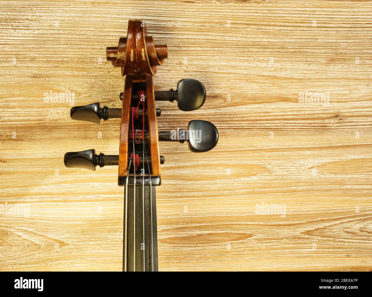 Hals und Kopfplatte eines Cellos mit einem texturierten Holzhintergrund und warmem Licht. Stockfoto