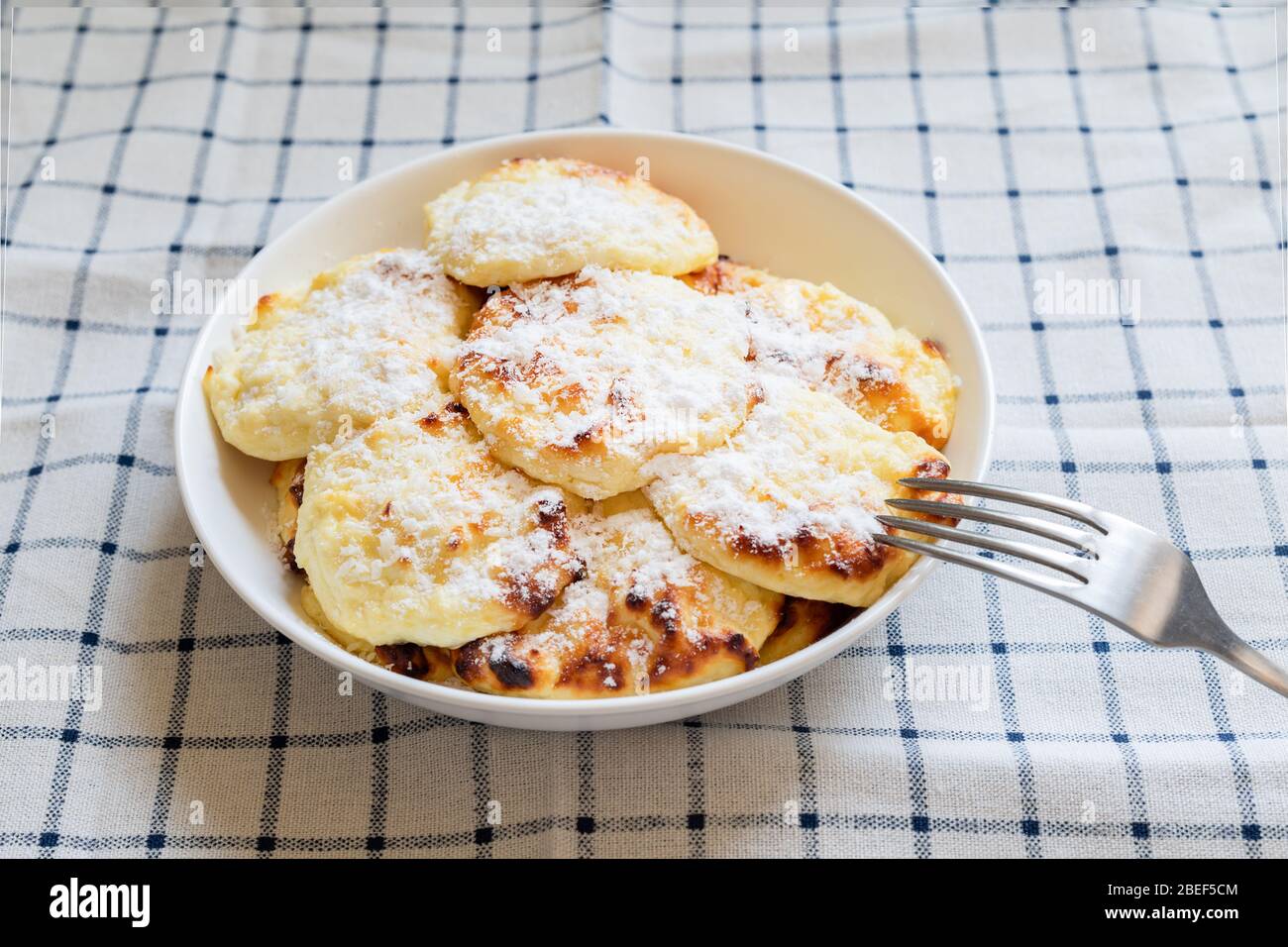 Einfaches Frühstück für Kinder. Süße Quark-Pfannkuchen auf einem weißen Teller, bestreut mit Puderzucker. Stockfoto