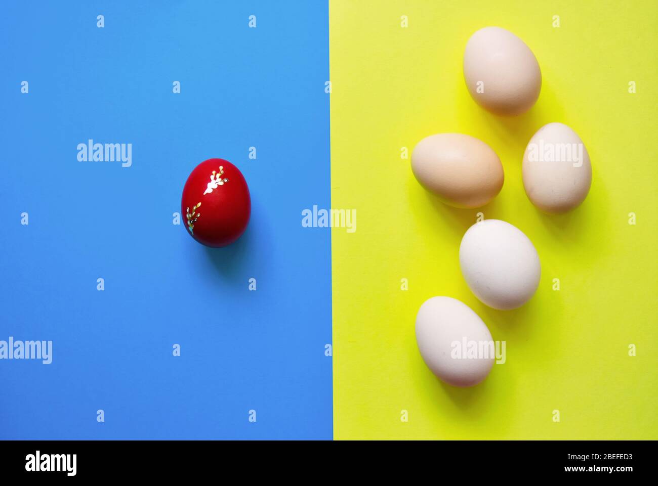 Weiße Ostereier auf blauem und gelbem Hintergrund mit einem roten Ei. Stockfoto Weiße Ostereier auf blauem und gelbem Hintergrund mit einem roten Ei. Stockfoto