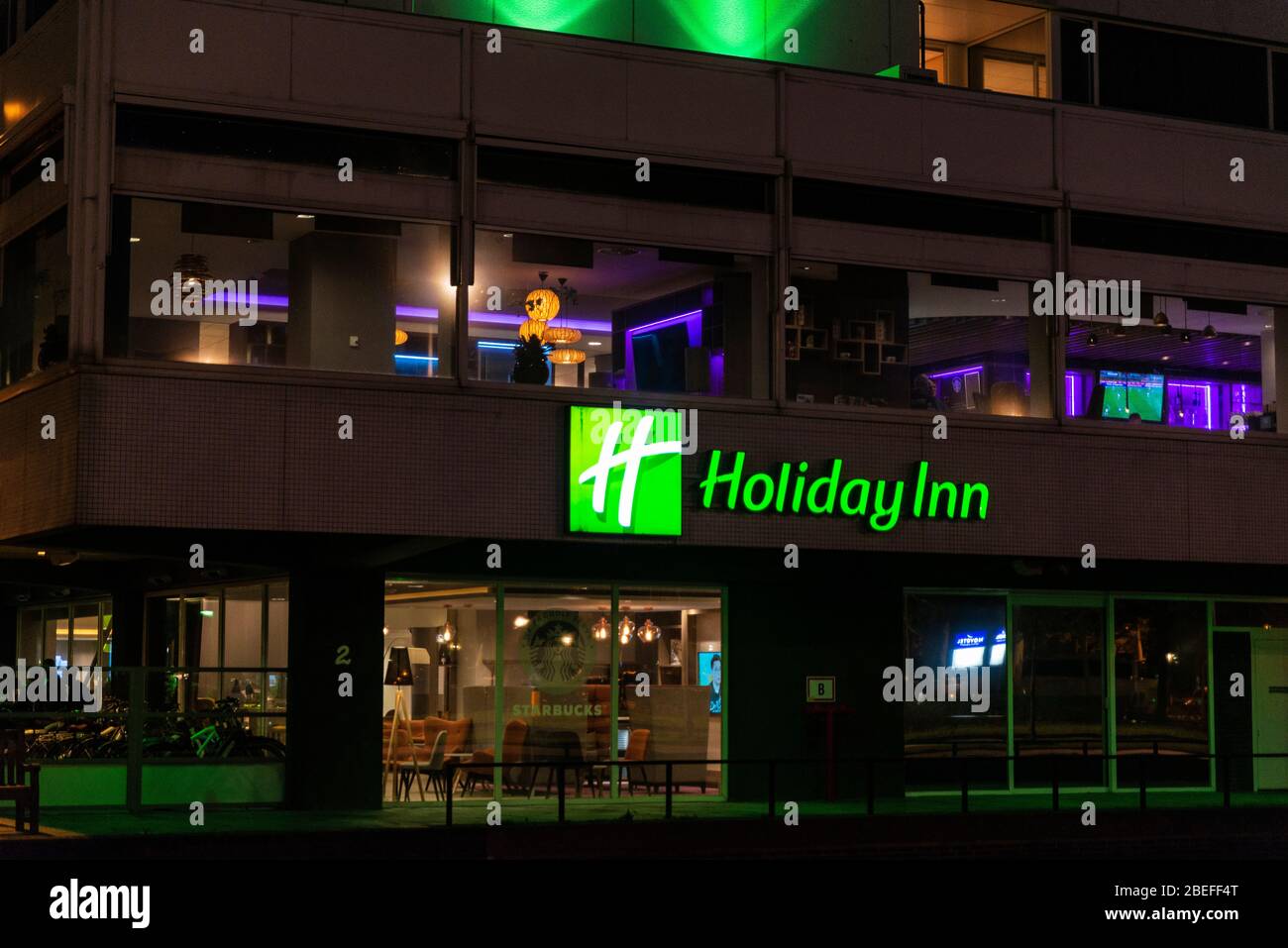 Amsterdam, Niederlande - 7. September 2018: Fassade des Holiday Inn Hotels und Starbucks Cafe bei Nacht in Amsterdam, Niederlande Stockfoto