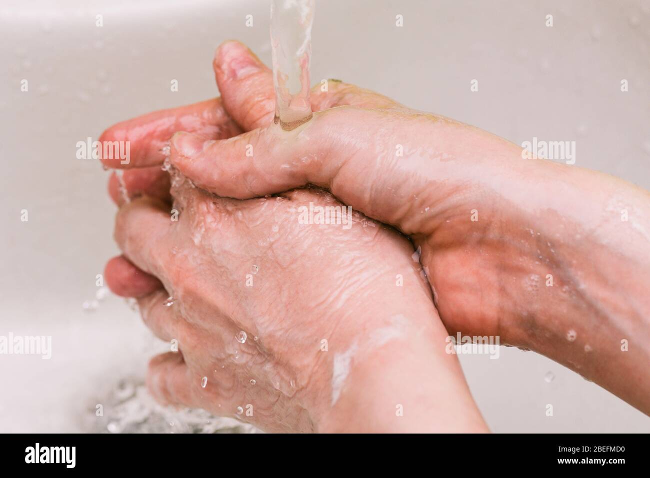 Die Hand des Mannes unter dem Wasserhahn mit Wasser. Hände nass machen und Wasser sprühen. Persönliche Hygiene und Prävention von Coronavirus-Krankheit Stockfoto