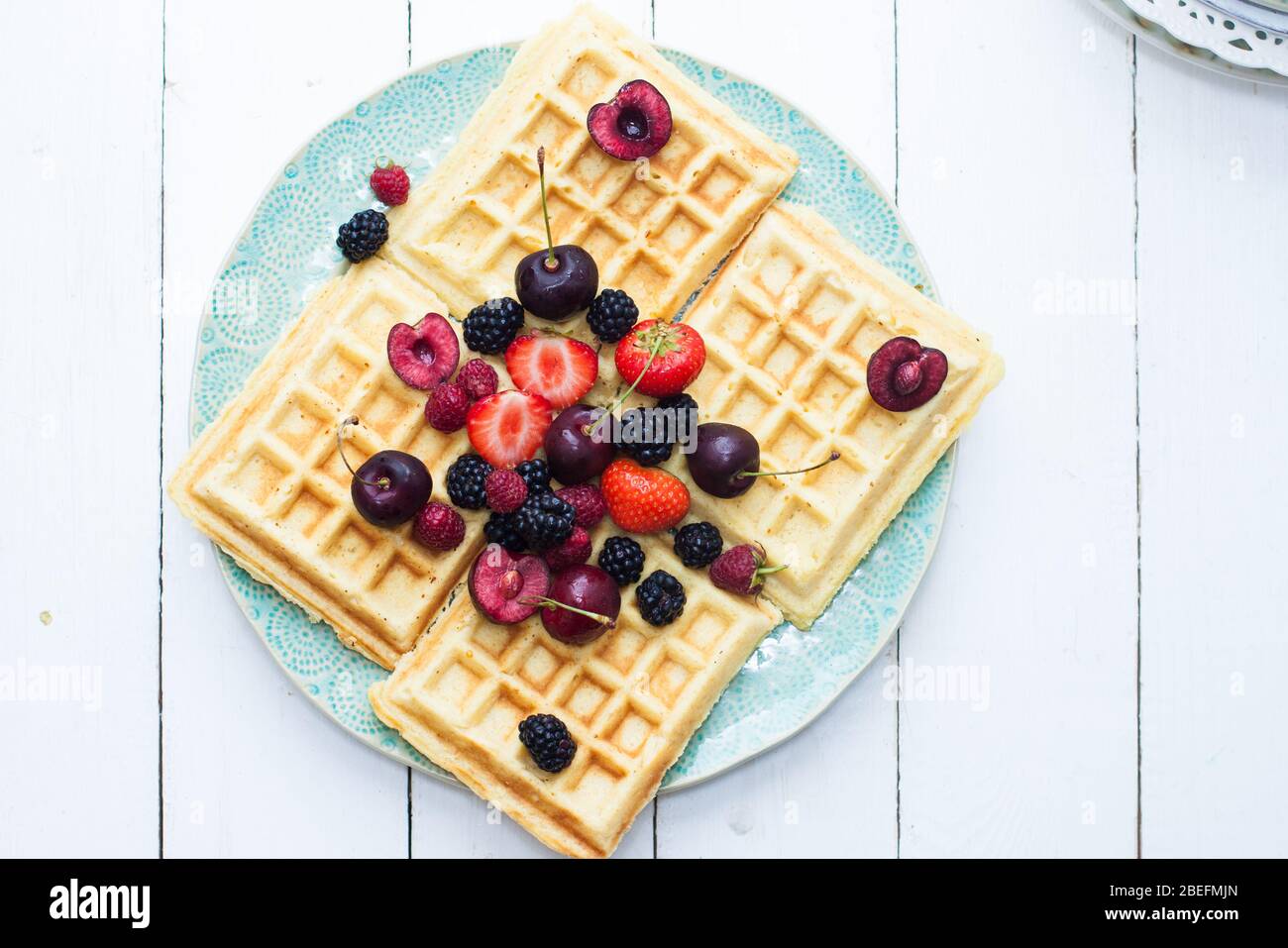 Belgische Waffeln mit Erdbeere, Kirsche, Heidelbeere auf blauem Teller. Weißer Hintergrund. Draufsicht. Stockfoto