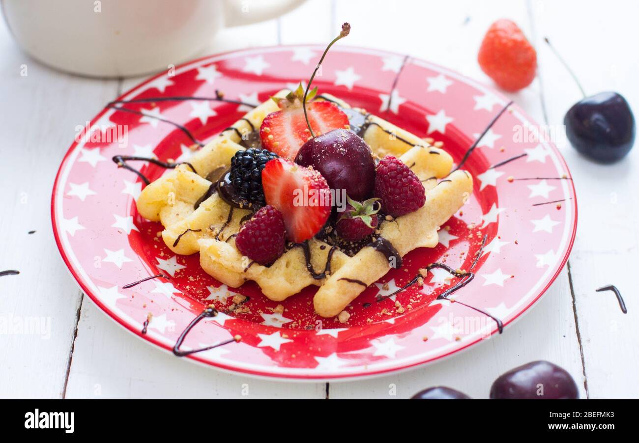 Belgische Waffeln mit Erdbeere, Kirsche, Heidelbeere auf rotem Teller mit Sternen. Weißer Hintergrund. Draufsicht. Stockfoto
