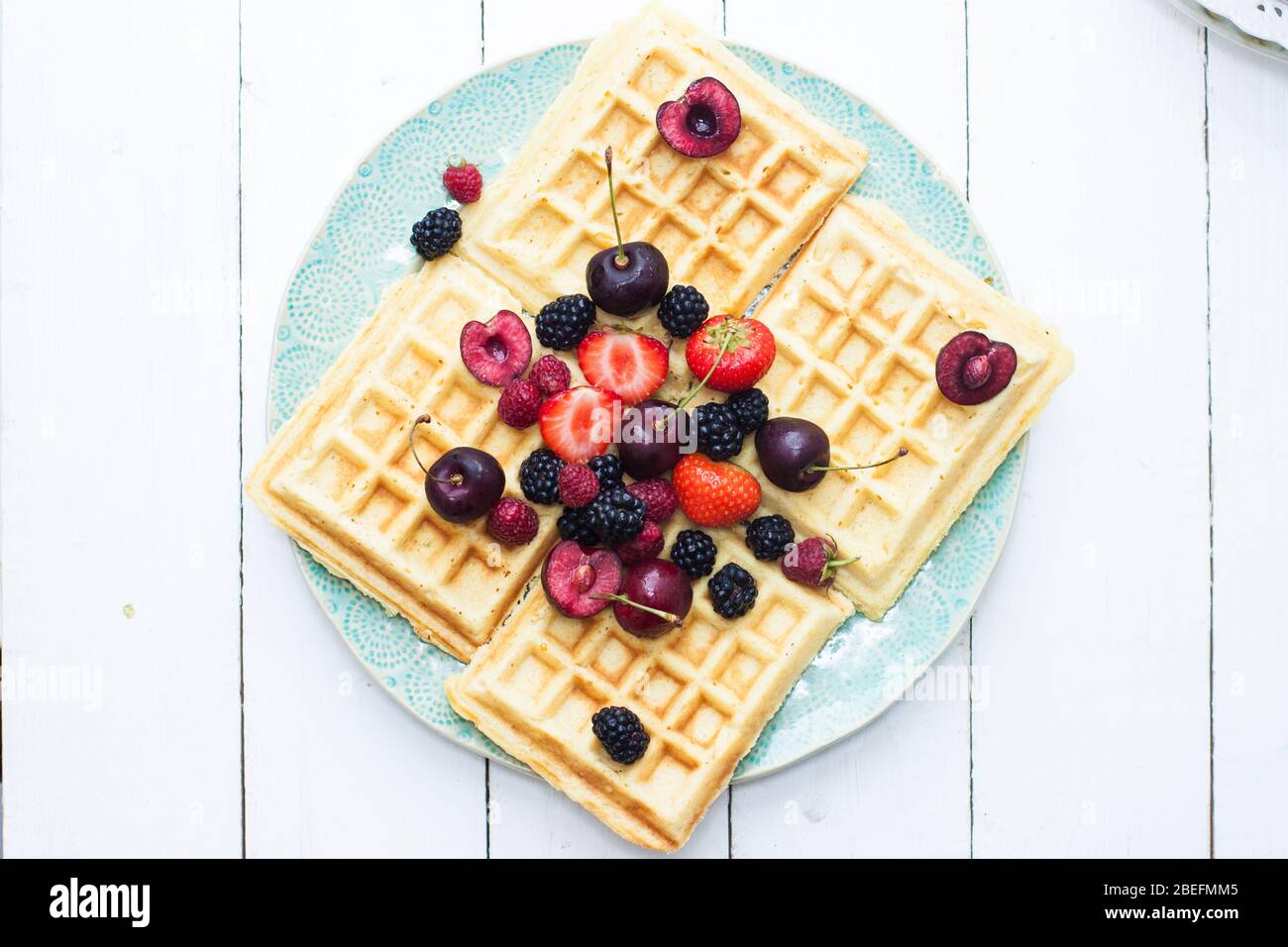 Belgische Waffeln mit Erdbeere, Kirsche, Heidelbeere auf blauem Teller. Weißer Hintergrund. Draufsicht. Stockfoto