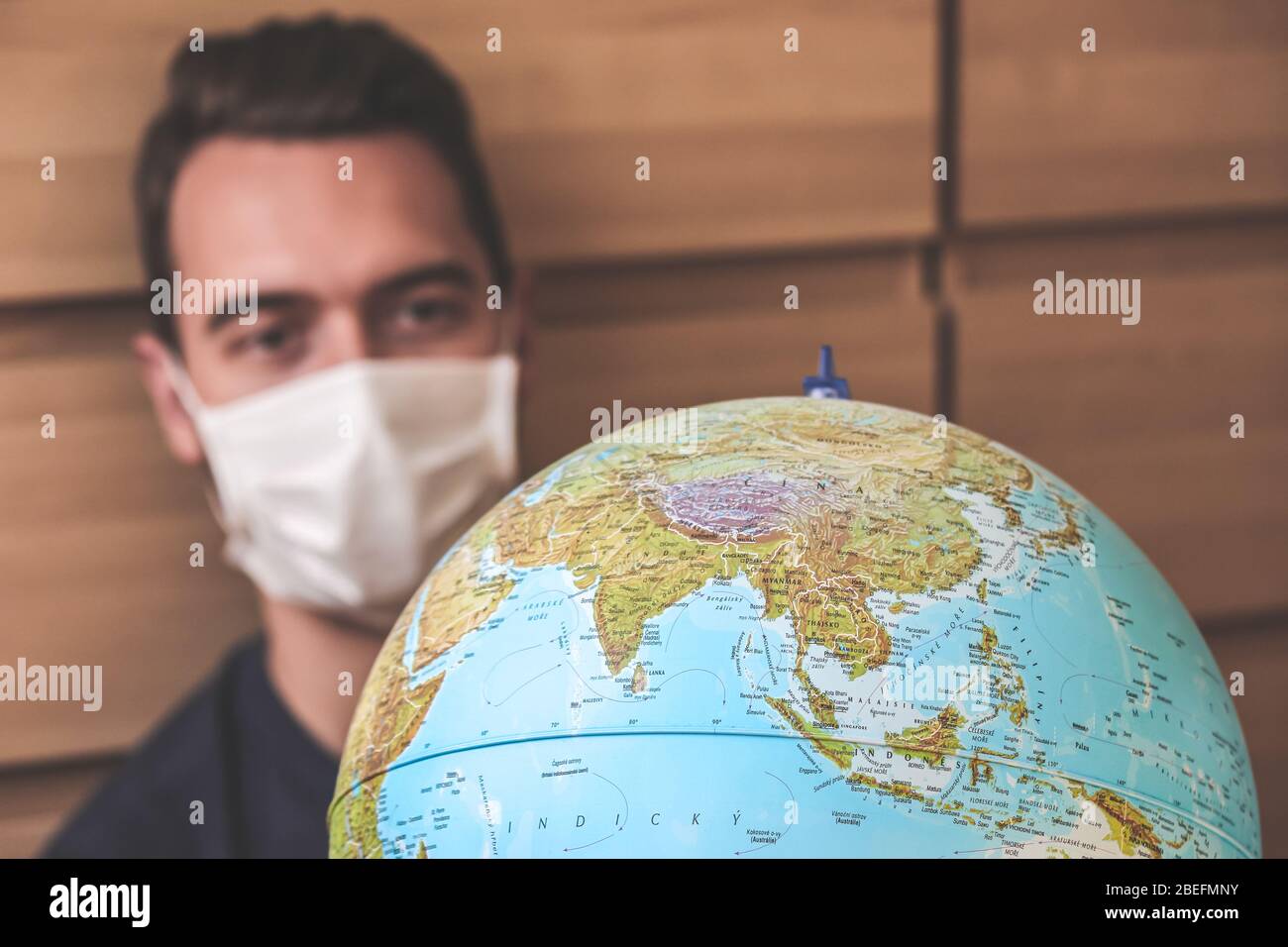 Verschwommener junger Mann Reisender in medizinischen Gesichtsmaske Blick auf Welt Globus. Quarantäne des Coronavirus. Reisebeschränkungen aufgrund des Ausbruchs der COVID-19. Reisen storniert. Selektiver Fokus. Stockfoto