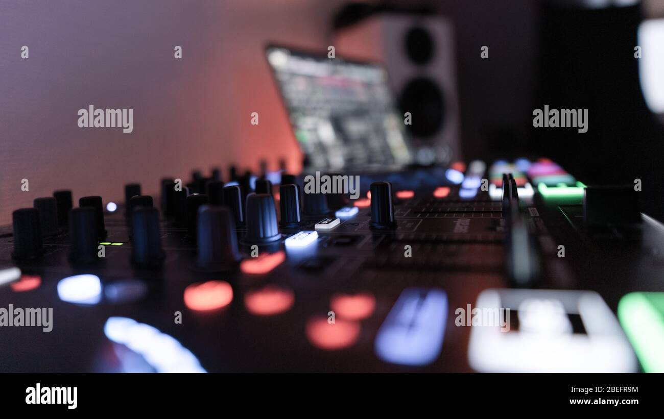 Seitenansicht eines beleuchteten DJ-Controllers mit Laptop und Lautsprecher im Hintergrund Stockfoto