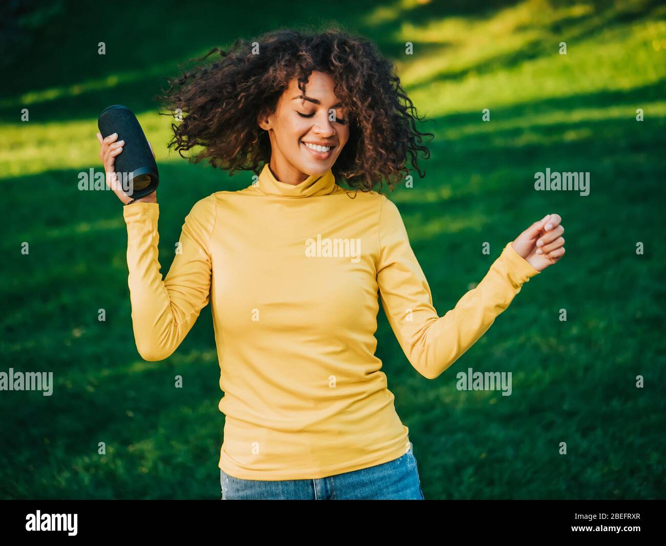 Moderne trendy afroamerikanischen Mädchen hören Musik von drahtlosen tragbaren speaker.Young schöne Frau genießen, tanzen im Park. Stockfoto